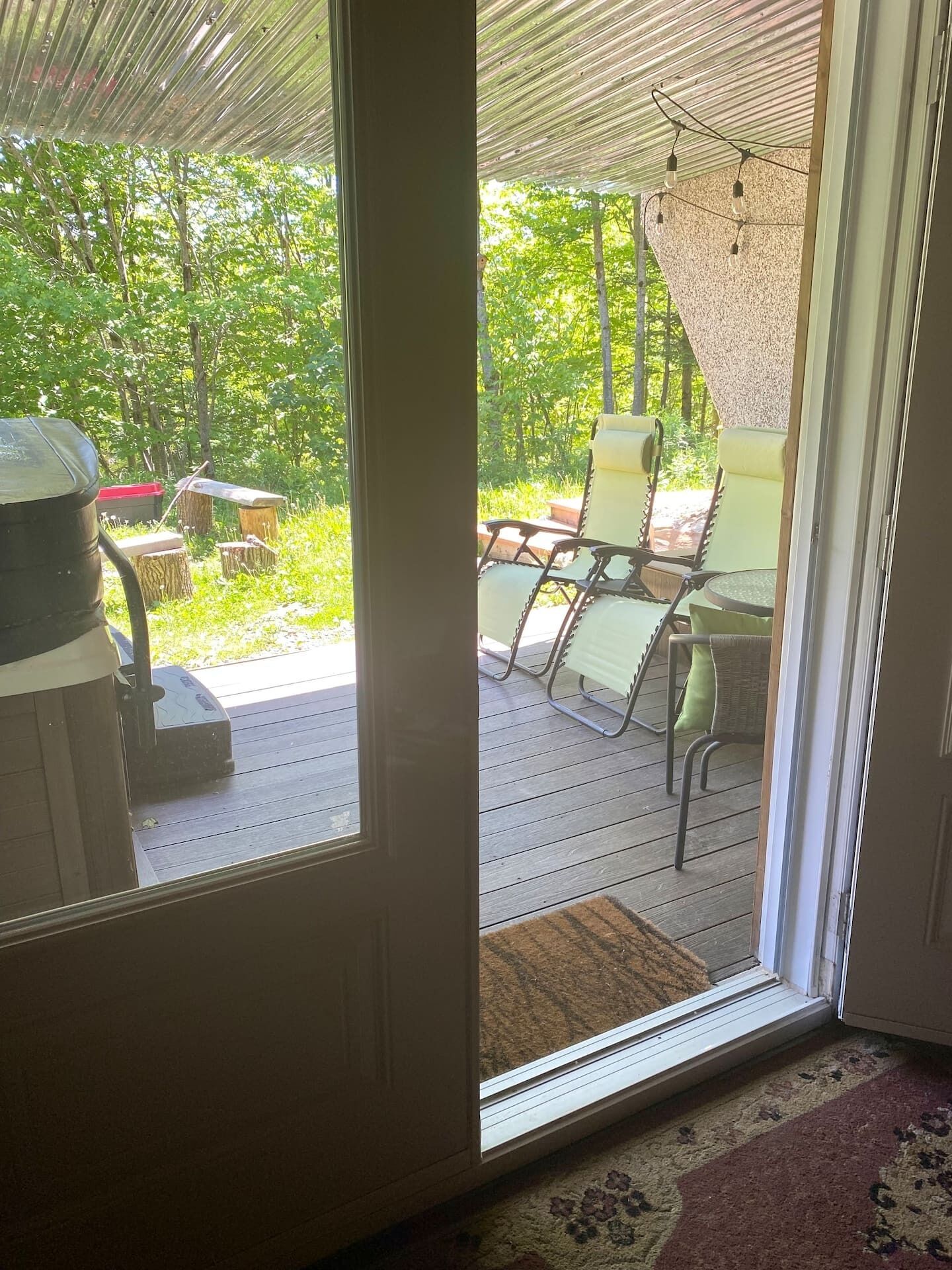 Un patio techado con mesa y sillas, una parrilla y vistas a una zona boscosa.