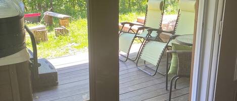 Un patio techado con mesa y sillas, una parrilla y vistas a una zona boscosa.