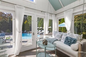 A sunlit room with a pool view, a sofa with decorative pillows, and a glass table with a centerpiece. - Glamorous Cabana (Newbury)