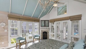 Une chambre spacieuse avec un grand lit, une cheminée et une vue sur l’extérieur grâce à de nombreuses fenêtres.