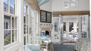 Une pièce lumineuse, baignée de soleil, avec de grandes fenêtres, une table en verre, une cheminée et une vue sur une piscine extérieure.