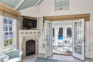 A room with a fireplace, a television, and a view of an outdoor swimming pool. - Glamorous Cabana (Newbury)