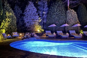A swimming pool with lounge chairs and umbrellas, surrounded by trees and a stone wall. - Glamorous Cabana (Newbury)