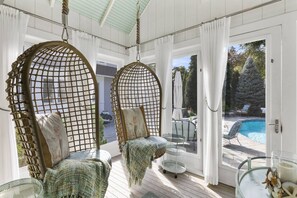 A sunlit room with two wicker chairs, a glass table, and a view of an outdoor swimming pool. - Glamorous Cabana (Newbury)