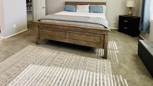 Een slaapkamer met een houten bed, een plafondventilator, een bedlamp en een kamerbreed tapijt met een patroon.
