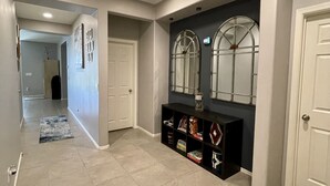 Een gang met een betegelde vloer, een zwarte console tafel met decoratieve objecten, en een grote spiegel met metalen frame.