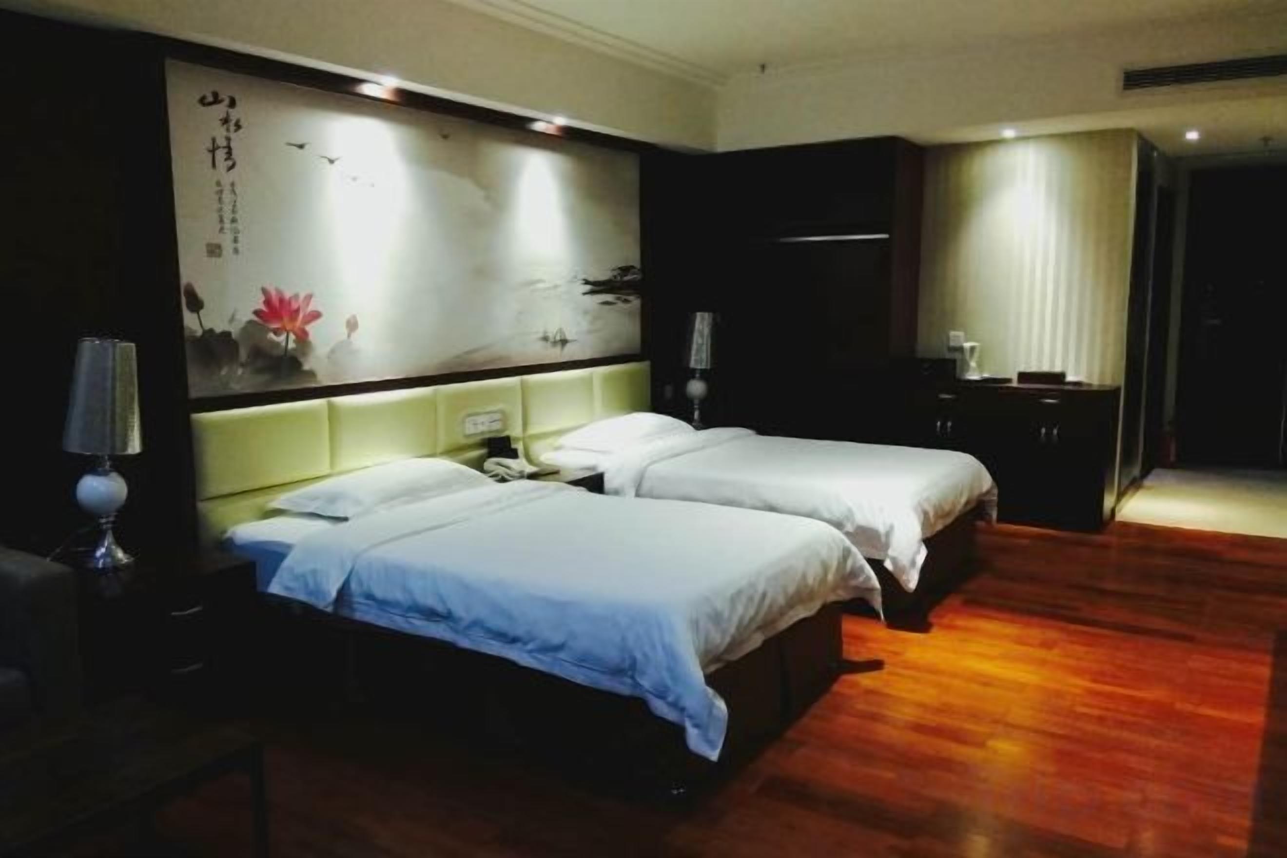 A hotel room with two beds, a nightstand, a lamp, and a wall with artwork.
