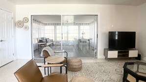 A living room with a brown leather sofa, a glass coffee table, a television on a stand, and a patterned rug. - Bohemian Bungalow on Byron Road (Fort Myers)