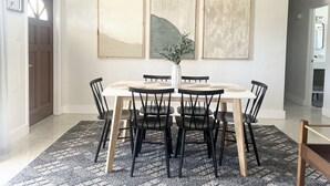 A dining area with a round table, black chairs, a woven pendant light, and three abstract paintings on the wall. - Bohemian Bungalow on Byron Road (Fort Myers)
