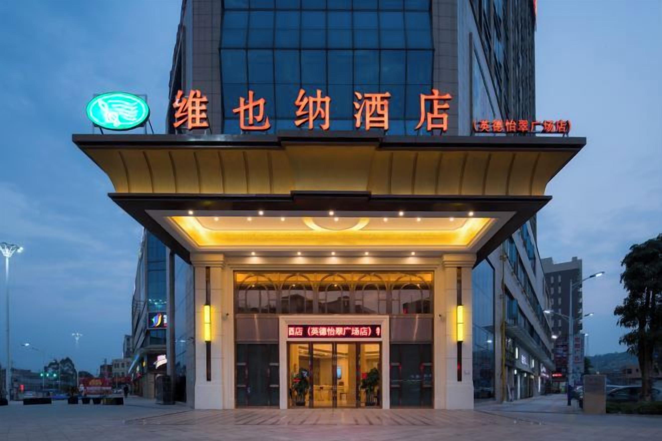 A hotel entrance with a neon sign, a large glass facade, and a sign indicating room availability.