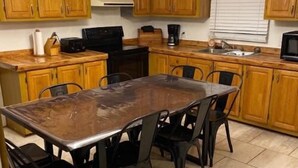 A kitchen with wooden cabinets, a large dining table with chairs, a microwave, and a coffee maker. - House 70 Oasis (Put-in-Bay)