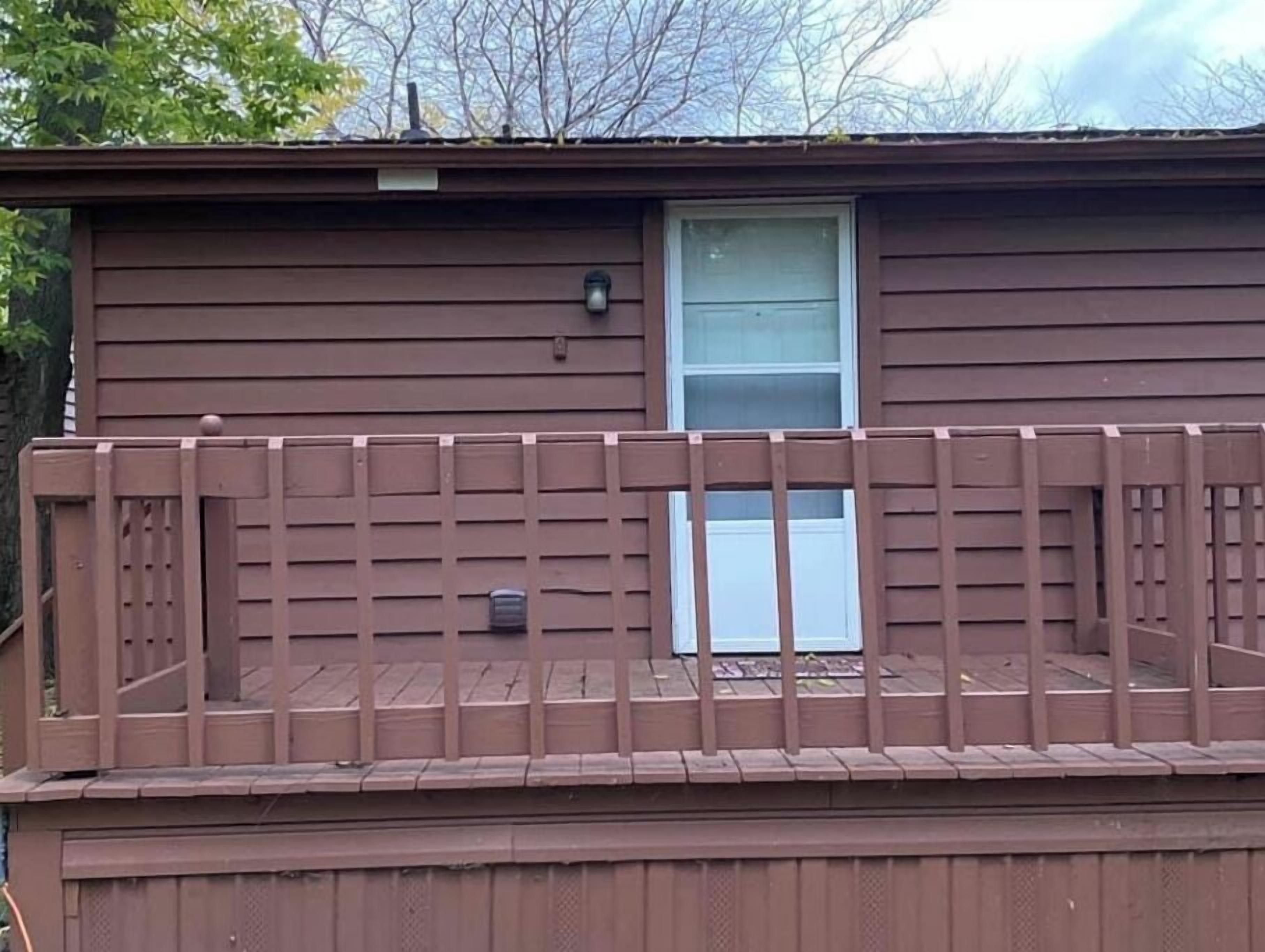 Una casa de un solo piso color café con una terraza de madera y una ventana.