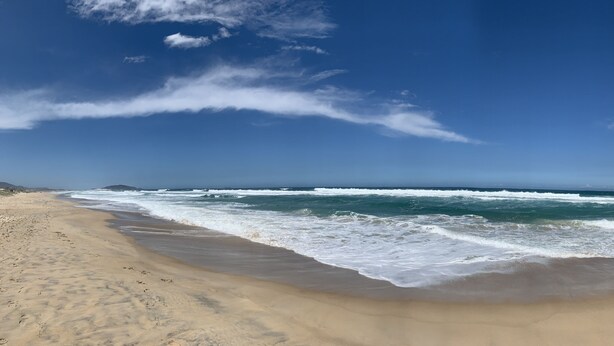 A beach with waves, a clear sky, and distant mountains. - Studio Amsterdã - Campeche-SC (Florianópolis)