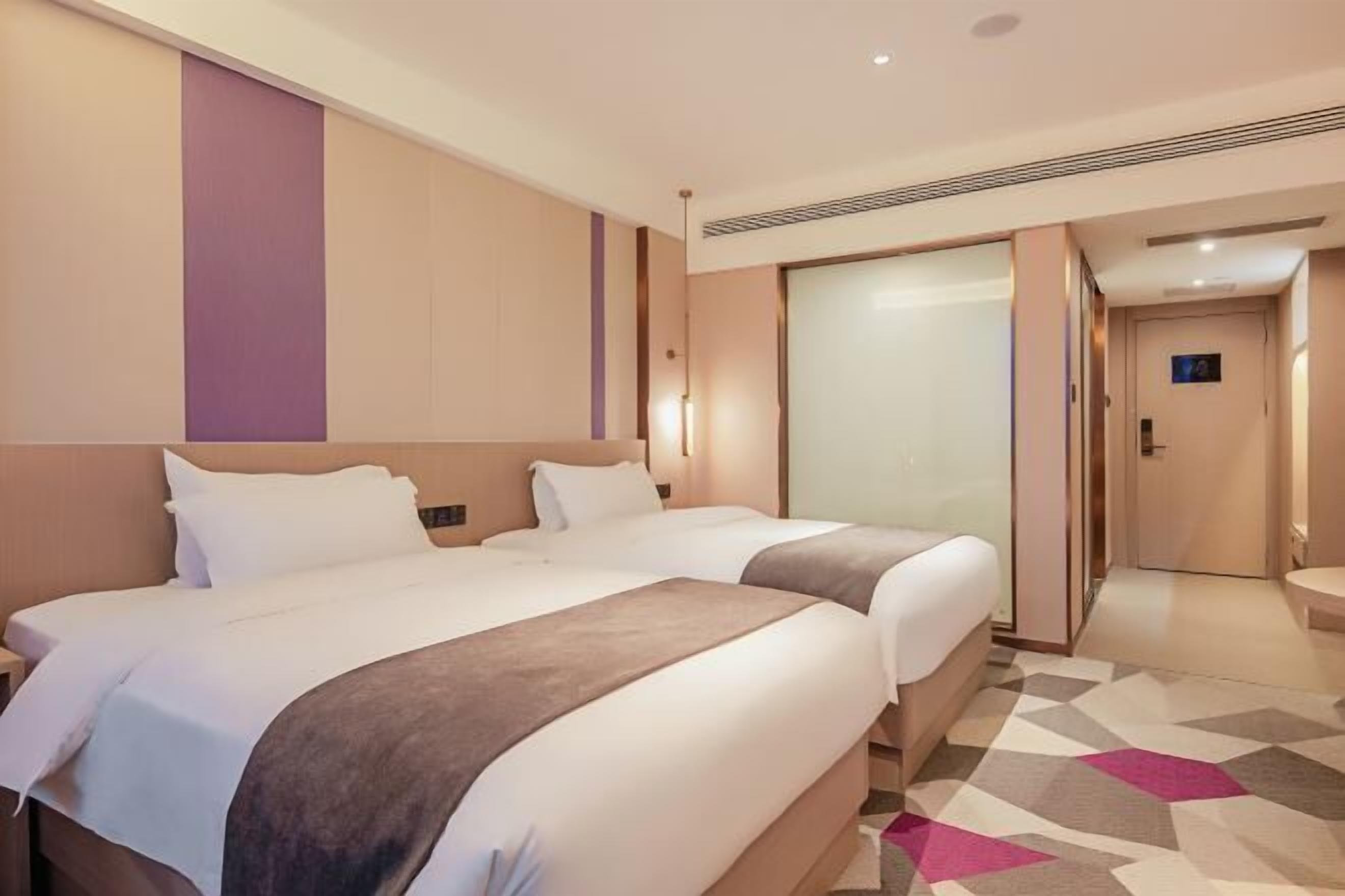A hotel room with two beds, a large window, and a door leading to a bathroom.