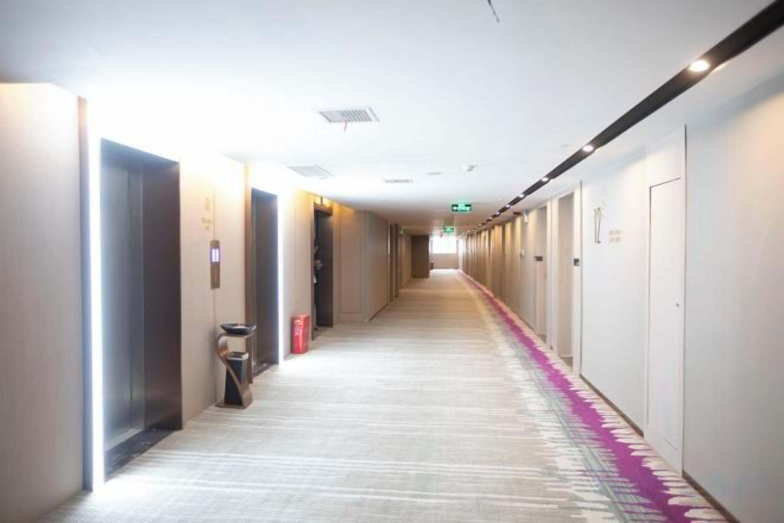 Un couloir d’hôtel avec des portes des deux côtés, une poubelle et un extincteur.