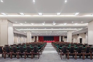 A conference room with rows of chairs, a stage with a red curtain, and a carpeted floor.