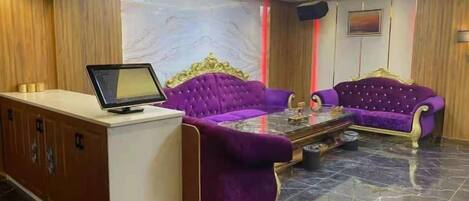 Un espace d’accueil comprenant un comptoir de réception, deux canapés violets, une table basse en verre et un mur en marbre.