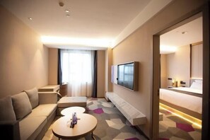 A hotel room with a sofa, a small table, a TV, and a bed.