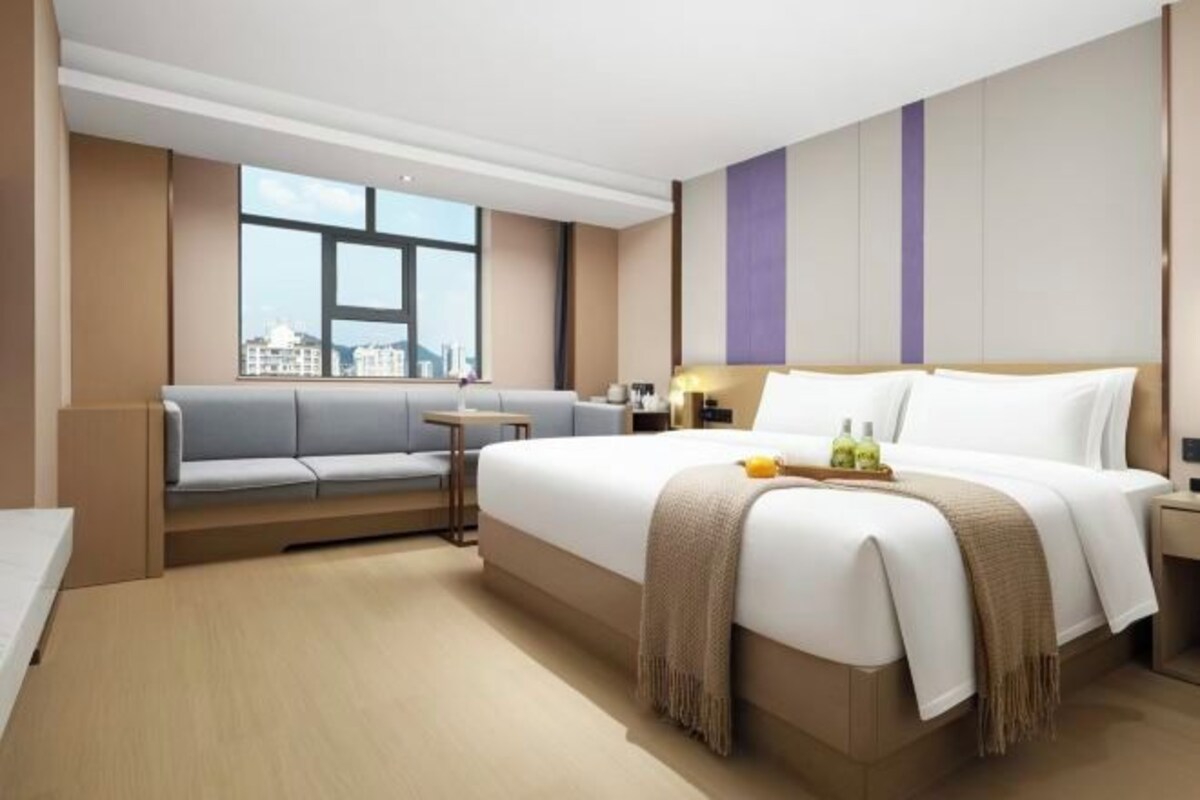 A hotel room with a large bed, a seating area, a small table, and a window with a city view.