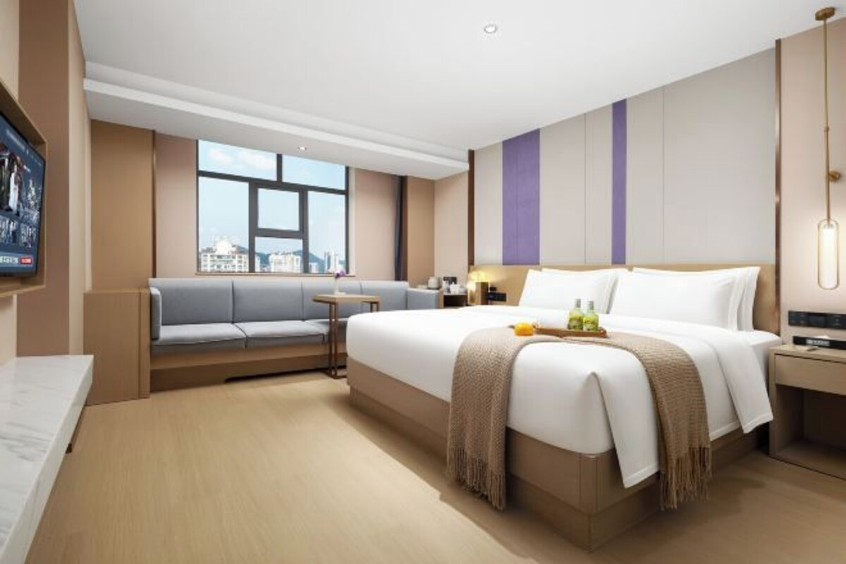 A modern hotel room with a large bed, a sofa, a desk, and a city view.