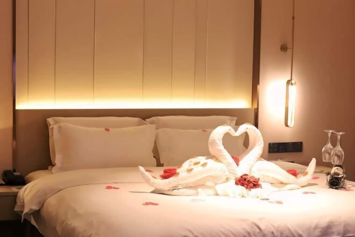 A hotel room with a bed, pillows, a wall-mounted light, and a decorative swan made of towels.