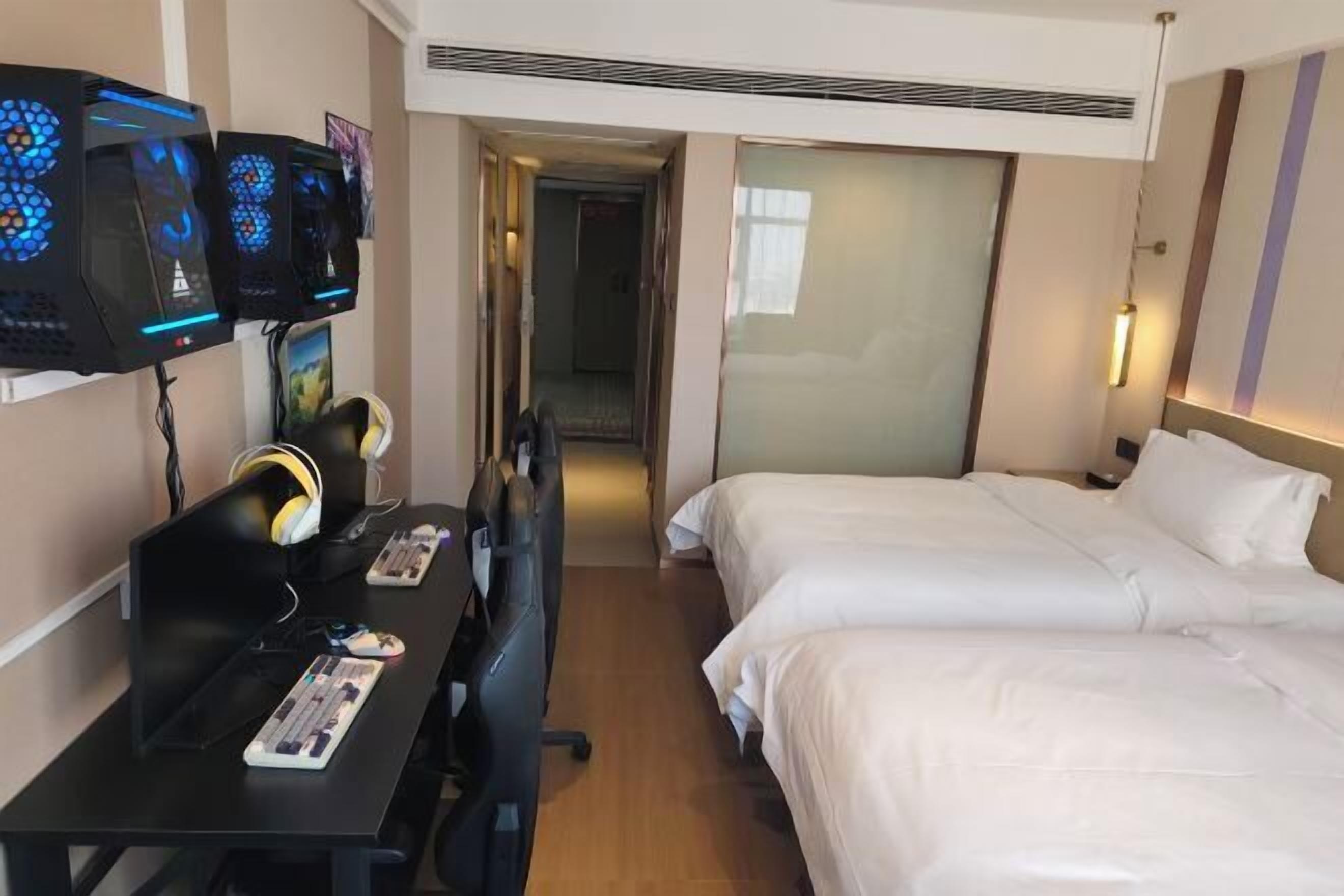 Une chambre d’hôtel avec deux lits, un bureau équipé d’un ordinateur et d’un clavier, et trois écrans fixés au mur.