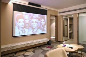A hotel room with a large screen displaying an image, a marble bench, a round table with a bottle and a remote control, and a mirror cabinet. - Xiangxiang Hotel (Xiangxiang)