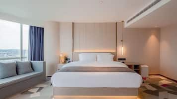 Quarto de hotel moderno com uma cama grande, um sofá, uma mesa de cabeceira e vista para a cidade.