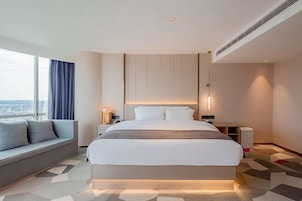 Habitación de hotel moderna con una cama grande, un sofá, una mesita de noche y vistas a la ciudad.