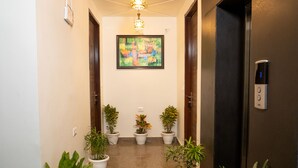 Un couloir agrémenté de plantes en pot, un luminaire au plafond et un écran numérique indiquant l’étage de l’ascenseur.