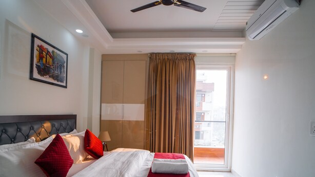 Une chambre d’hôtel avec un lit, un ventilateur de plafond, un climatiseur, une fenêtre avec des rideaux et un tableau au mur.
