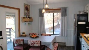 Et spiseområde med et bord dækket til fire personer, et vindue med gardiner, og et køkken med et køleskab.