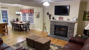Una sala de estar con chimenea, sofás de cuero, una zona de comedor con sillas y un televisor montado en la pared.
