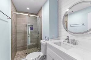 Un baño moderno con cabina de ducha de vidrio, un lavabo blanco y un espejo redondo.