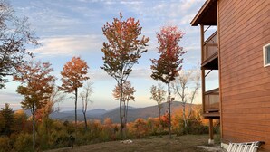 A wooden cabin with a balcony overlooking a grassy area with autumn trees and distant mountains. - Misty View (Rumney)