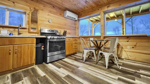 A wooden cabin kitchen with a stove, sink, and dining table with chairs. - Misty View (Rumney)