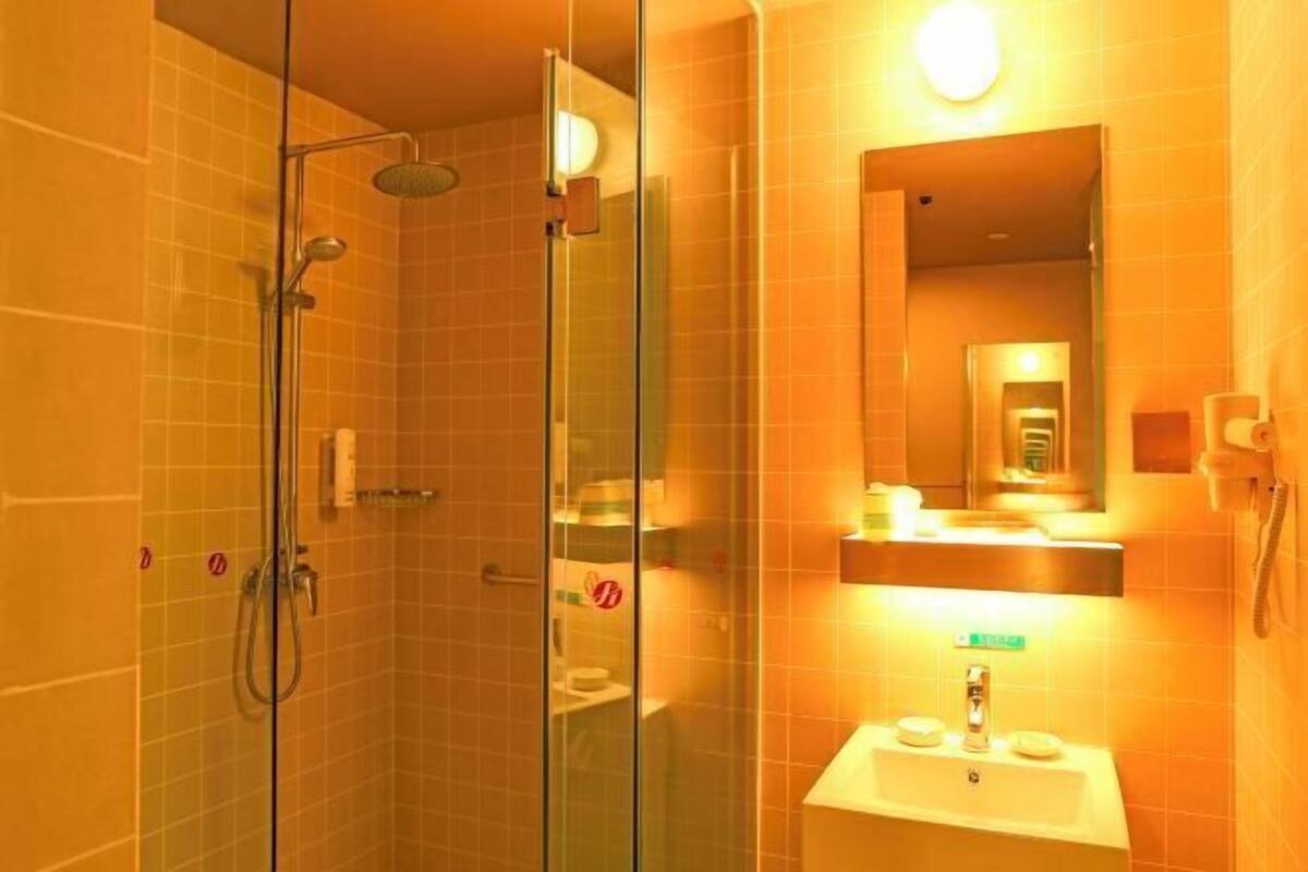 A glass-enclosed shower with a handheld showerhead, a sink with a mirror above it, and a toilet visible through the glass.