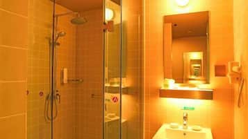 A glass-enclosed shower with a handheld showerhead, a sink with a mirror above it, and a toilet visible through the glass.