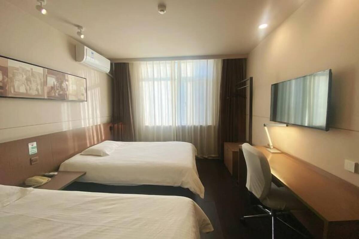 A hotel room with two beds, a desk, a chair, a TV, and a window with curtains.
