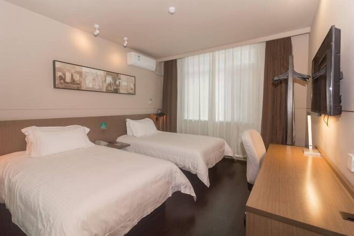 A hotel room with two beds, a desk, a TV, and a window with curtains.