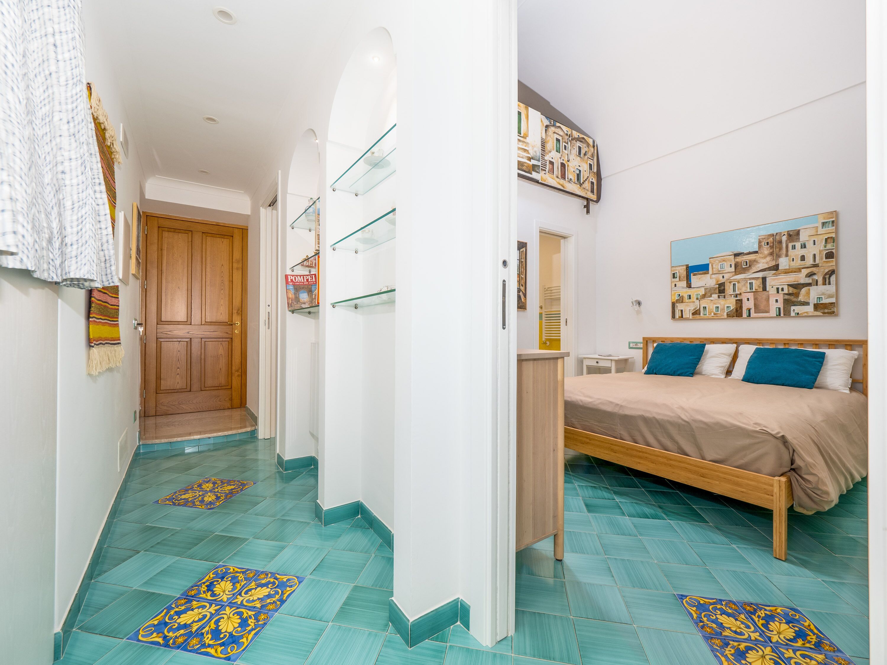 Habitació d'hotel amb un llit, un armari de fusta, una cabina de dutxa de vidre i un passadís amb rajoles estampades.