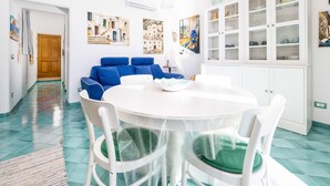 Ein helles, modernes Wohnzimmer mit einem runden Esstisch, weißen Stühlen und einem blauen Sofa.