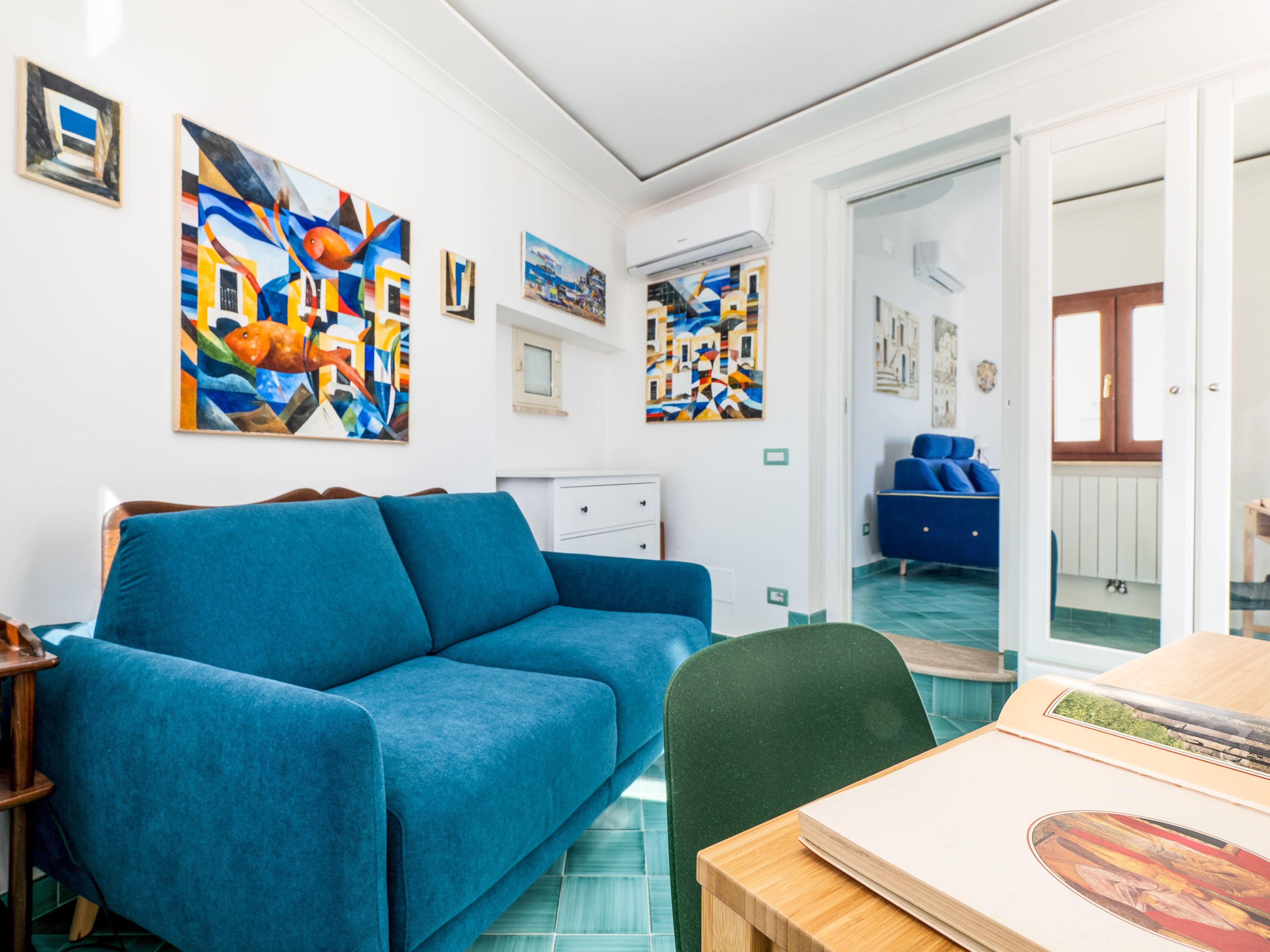 Un soggiorno moderno con un divano blu, un tavolo in legno e quadri astratti colorati alle pareti.