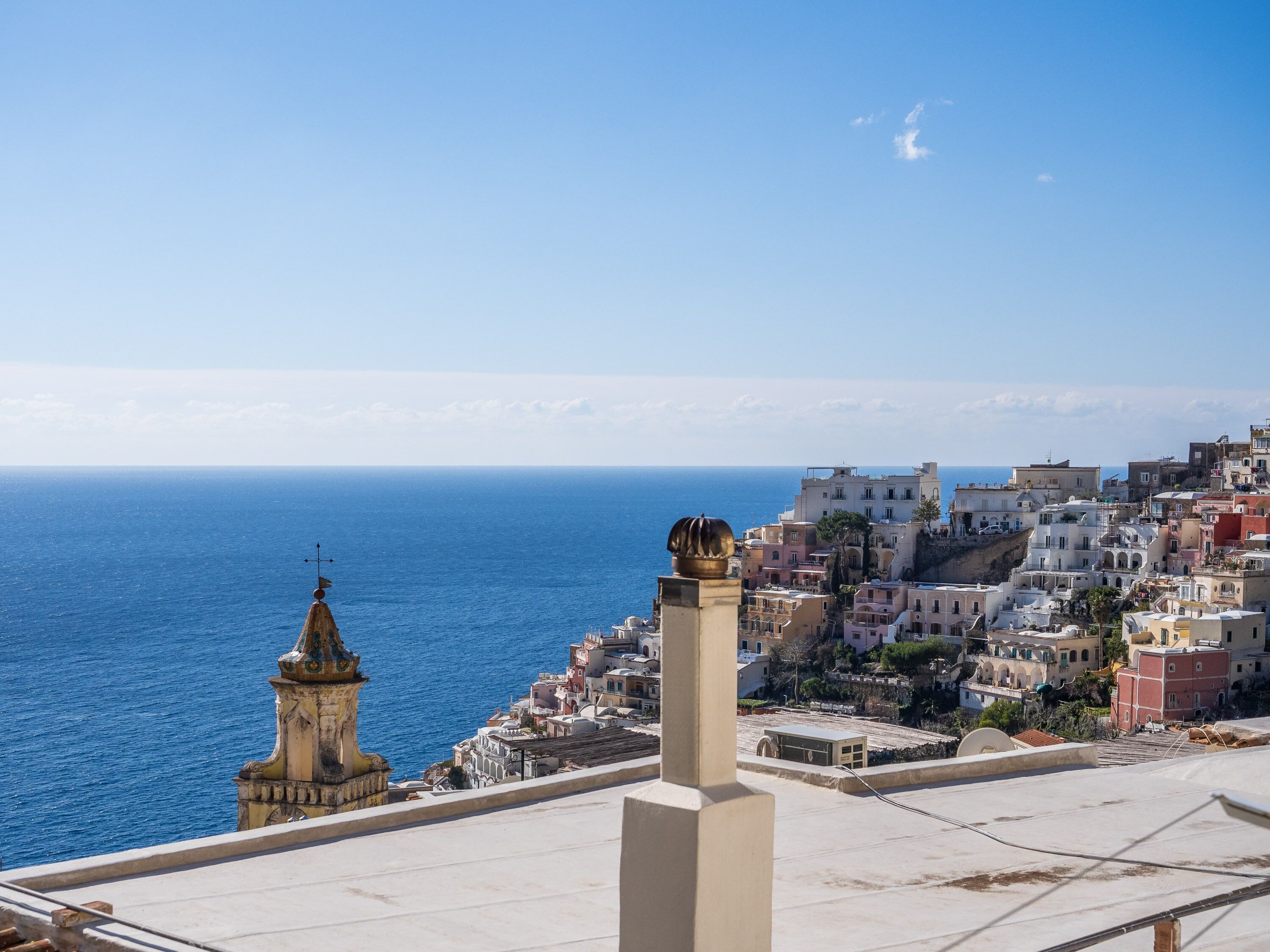 Un pueblo costero con edificios cerca del mar, una imponente torre dorada y un cielo azul despejado.