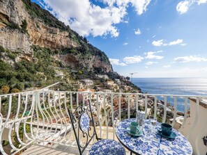A balcony with a table and chairs, overlooking a coastal town with buildings and cliffs. - Artist House in Positano (Positano)