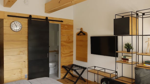 A bedroom with a bed, a sliding door, a TV, a shelf, and a clock. - The Vine on main  (Stamford)