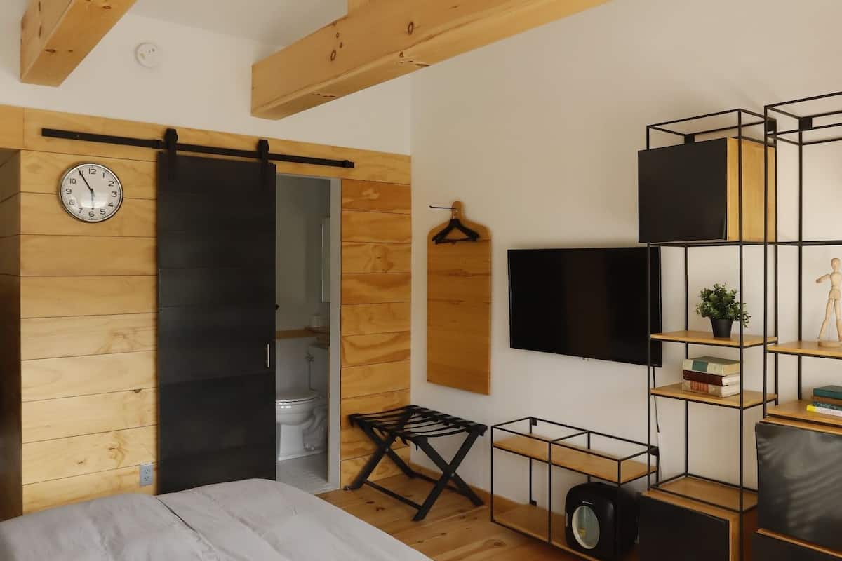 Quarto com cama, porta deslizante, televisão, prateleira e relógio.
