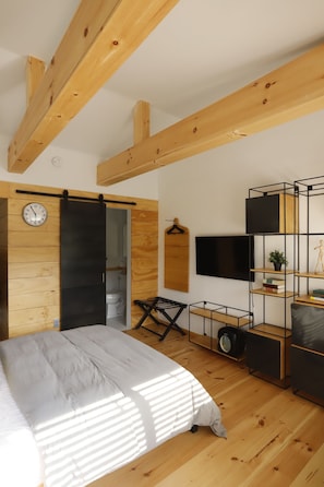 A bedroom with a bed, a sliding door, a TV, a shelf, and a clock. - The Vine on main  (Stamford)