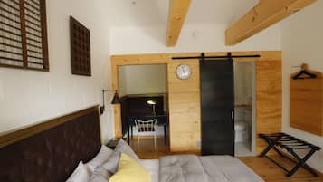 A bedroom with a bed, a wooden headboard, a wall clock, and a wooden door leading to another room.