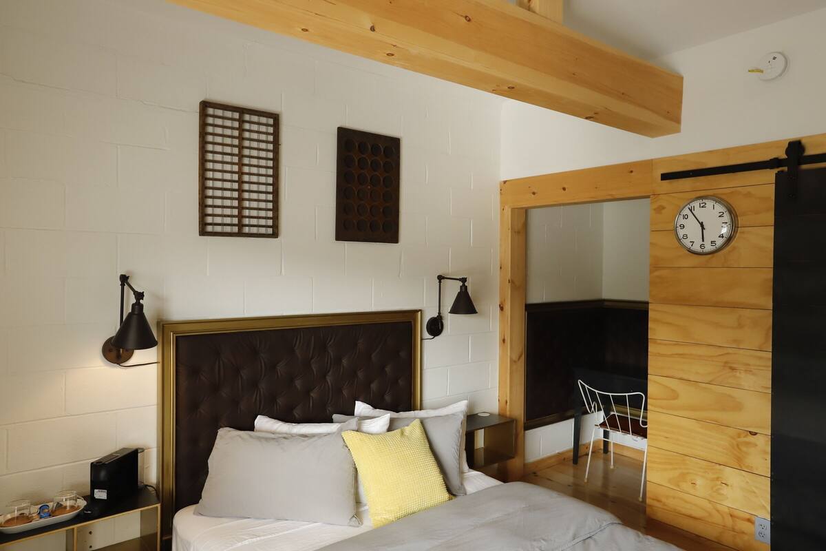Quarto com cama, mesas de cabeceira, um relógio e uma cadeira.